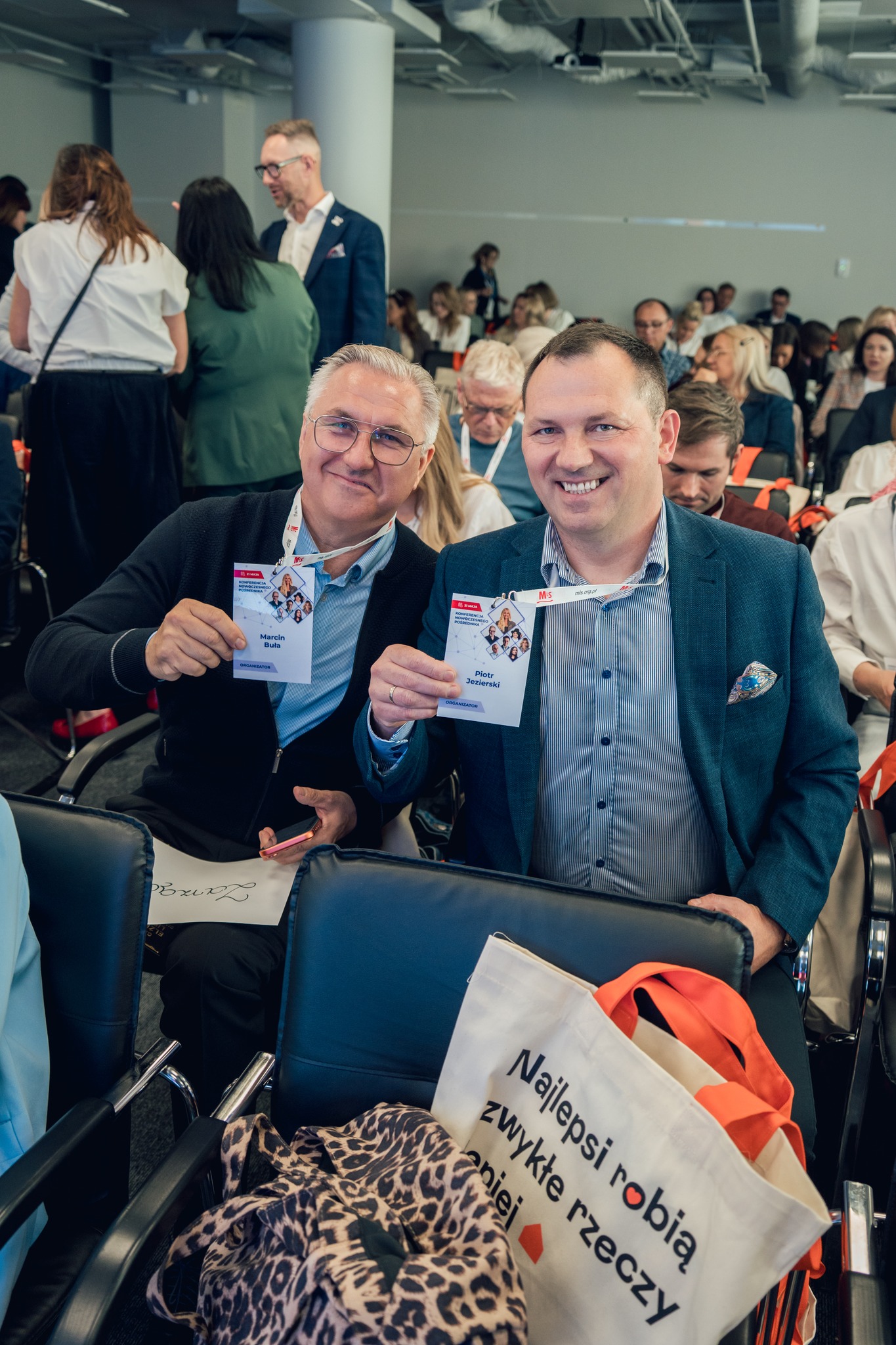 `Photo of MLS conference attendees sitting in rows and holding up their name badges towards the camera